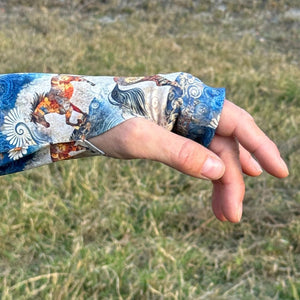 Hand with a colorful sleeve against a grassy background showing the thumb hole of the horse riding shirt