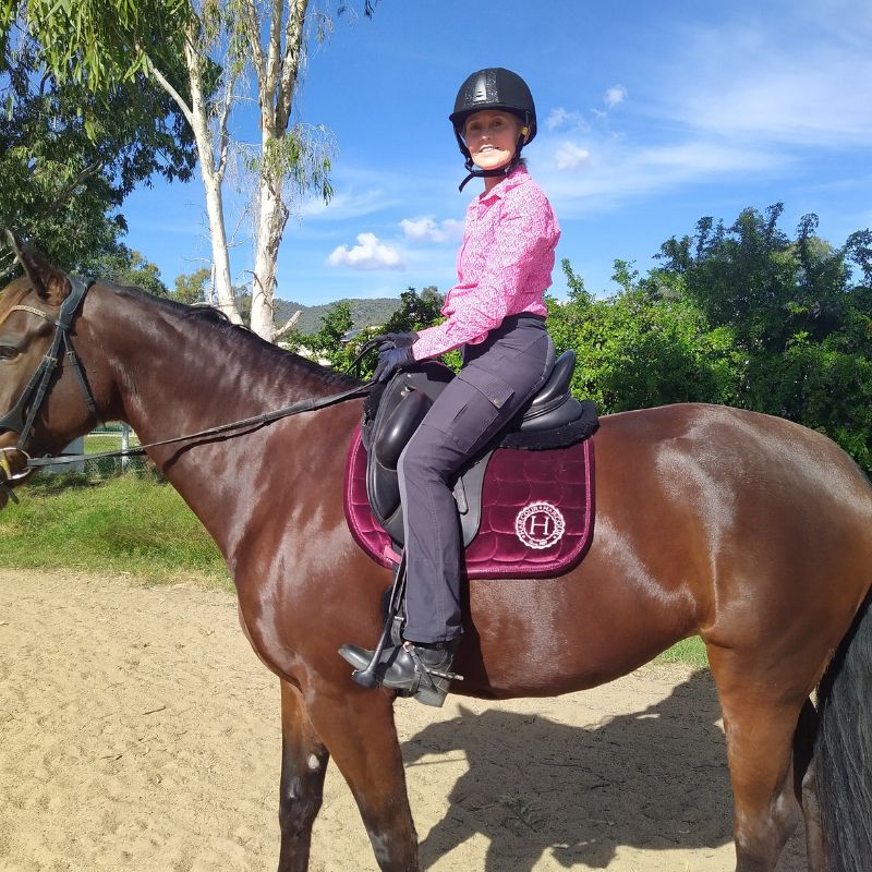 woman wearing pink top and trainer pants riding a brown horse