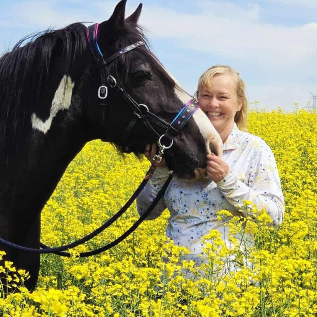 Woman wearing Ride Proud, Haven Riding Shirt smiling with black and white horse in bright yellow canola field