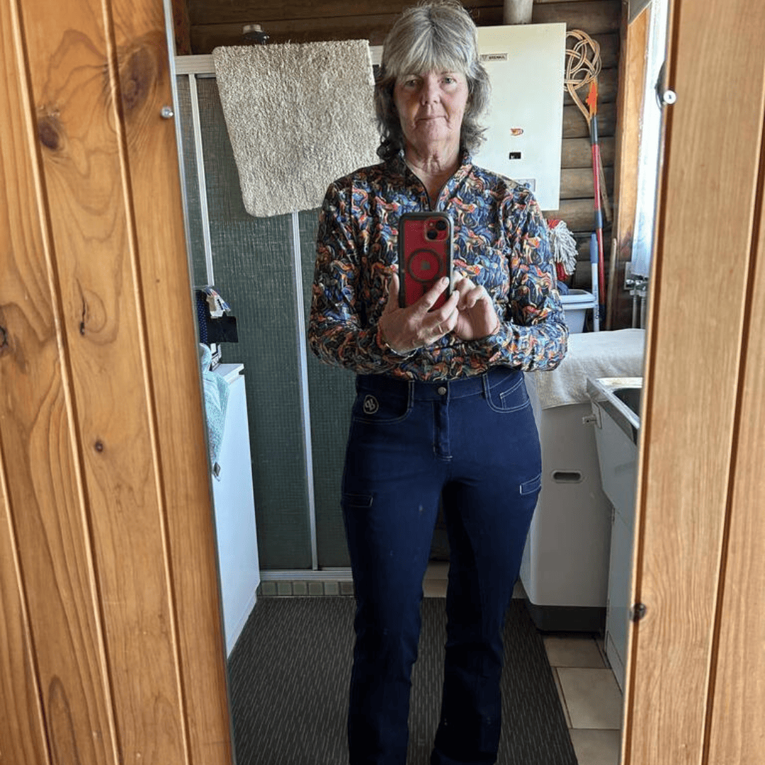 Person taking a mirror selfie wearing athe Kaleidoscope patterned shirt and Legend blue jeans from Ride Proud clothing in a home setting.