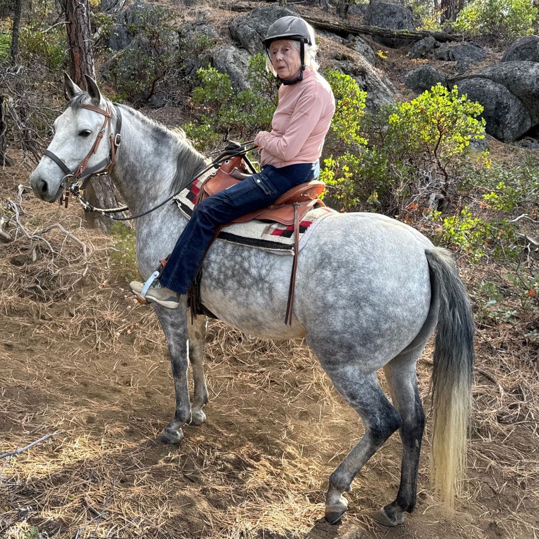 Mary K wearing Ride Proud Horizon Jeans, riding a grey horse in a  US Forest.