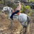 Mary K wearing Ride Proud Horizon Jeans, riding a grey horse in a  US Forest.