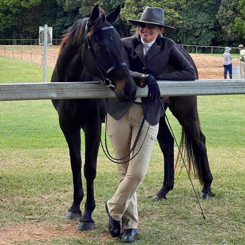 woman wearing a black hat and sunglasses standing beside a horse